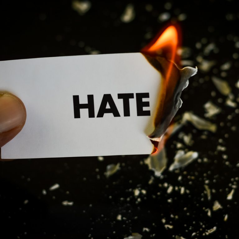 burning hate, human hand holding the word hate written on a paper burning with flame and ashes on a black background, concept