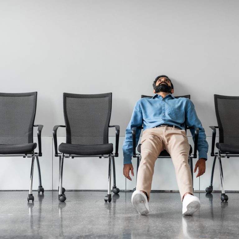 Bored and disappointed male indian employee sitting in waiting room on row of chairs, feeling tired and upset, full length shot, free space