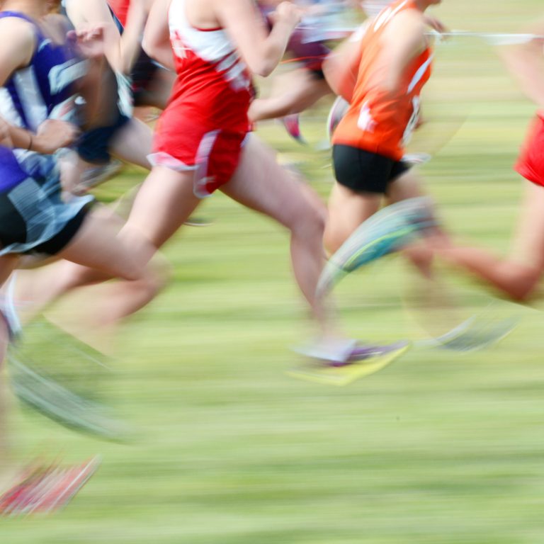 Several runners blurred with morion running a race on grass wearing red bibs team competition
