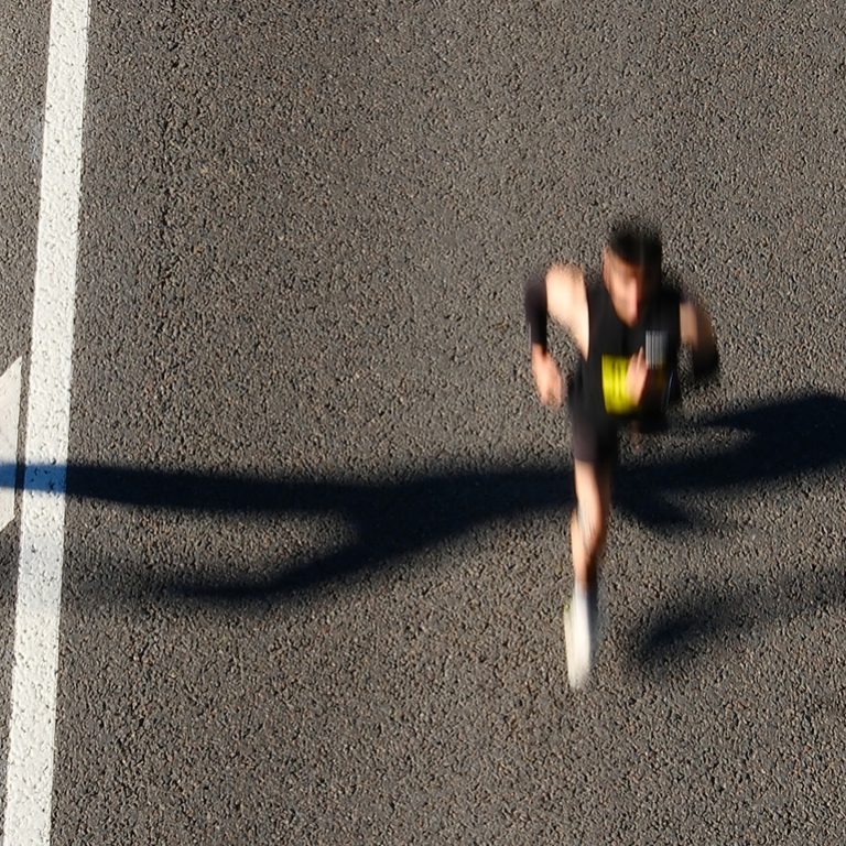 Aerial view of marathon runners on urban road with chevron markings, blurred motion capturing speed and movement of competitors