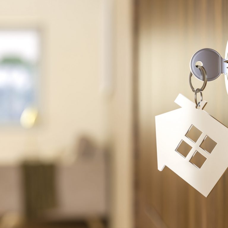 House key with a house shape keychain in a door lock, representing new home ownership