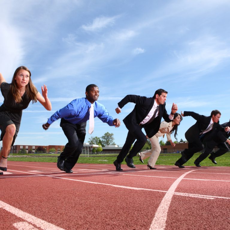 Group of people dressed in business attire racing on track.  Some slight motion blur on people.